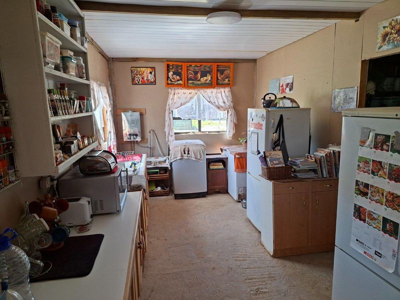 A functional kitchen area featuring built-in shelving and cabinetry, with a timber ceiling and window, requiring cosmetic updates to improve the overall finish.