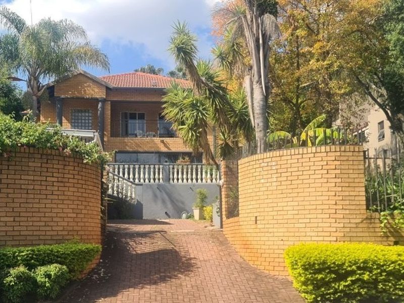 Front view of a double-story facebrick house featuring a paved driveway, brick boundary walls, and a balcony with a classic balustrade.