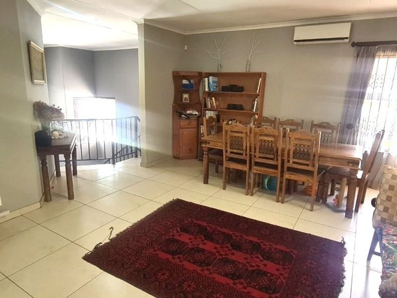 Spacious open-plan living and dining area featuring tiled flooring, a wall-mounted air conditioning unit, and direct access to a staircase.