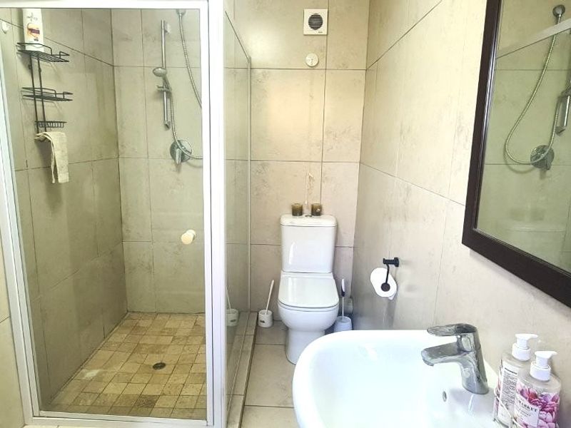 A functional bathroom featuring a walk-in shower with a glass enclosure, a pedestal basin, and neutral wall and floor tiling.