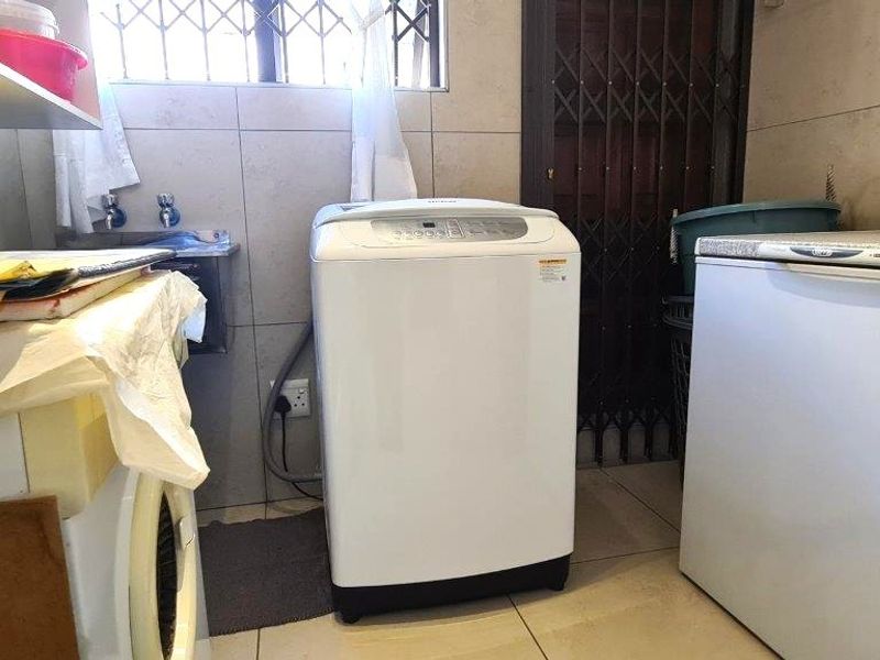 Functional laundry area featuring tiled walls and flooring, equipped with necessary plumbing connections and security features.