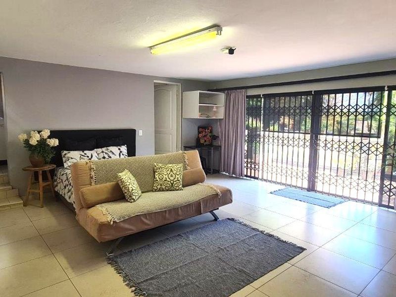 Spacious bedroom featuring tiled flooring, extensive built-in cupboards, and large sliding doors leading to the garden area.