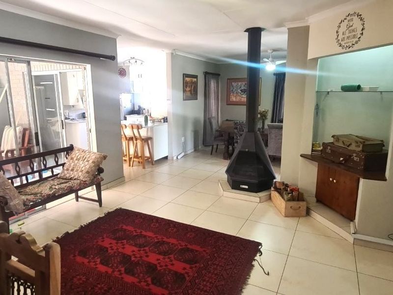 Spacious open-plan living area featuring a central freestanding fireplace, tiled flooring, and built-in display shelving, with seamless access to an enclosed patio.