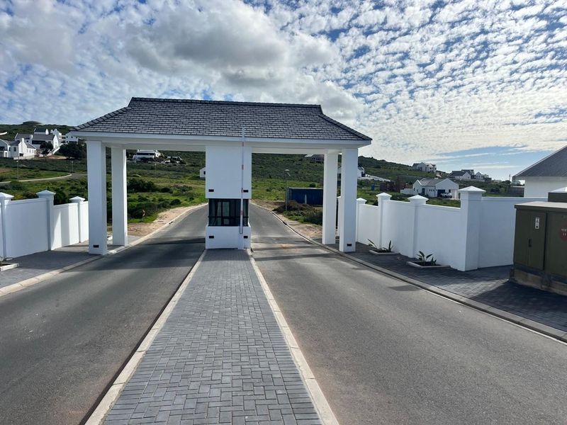 A well-maintained residential estate entrance featuring a modern security gatehouse, paved driveway, and perimeter boundary walls.