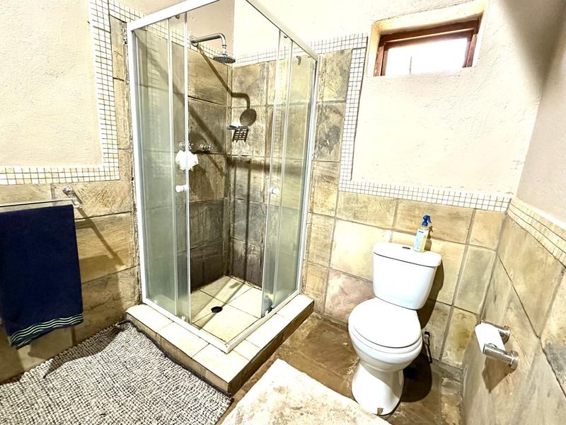 A functional bathroom featuring a glass-enclosed shower, toilet, and textured wall tiling. The space would benefit from cosmetic updates to finishes.