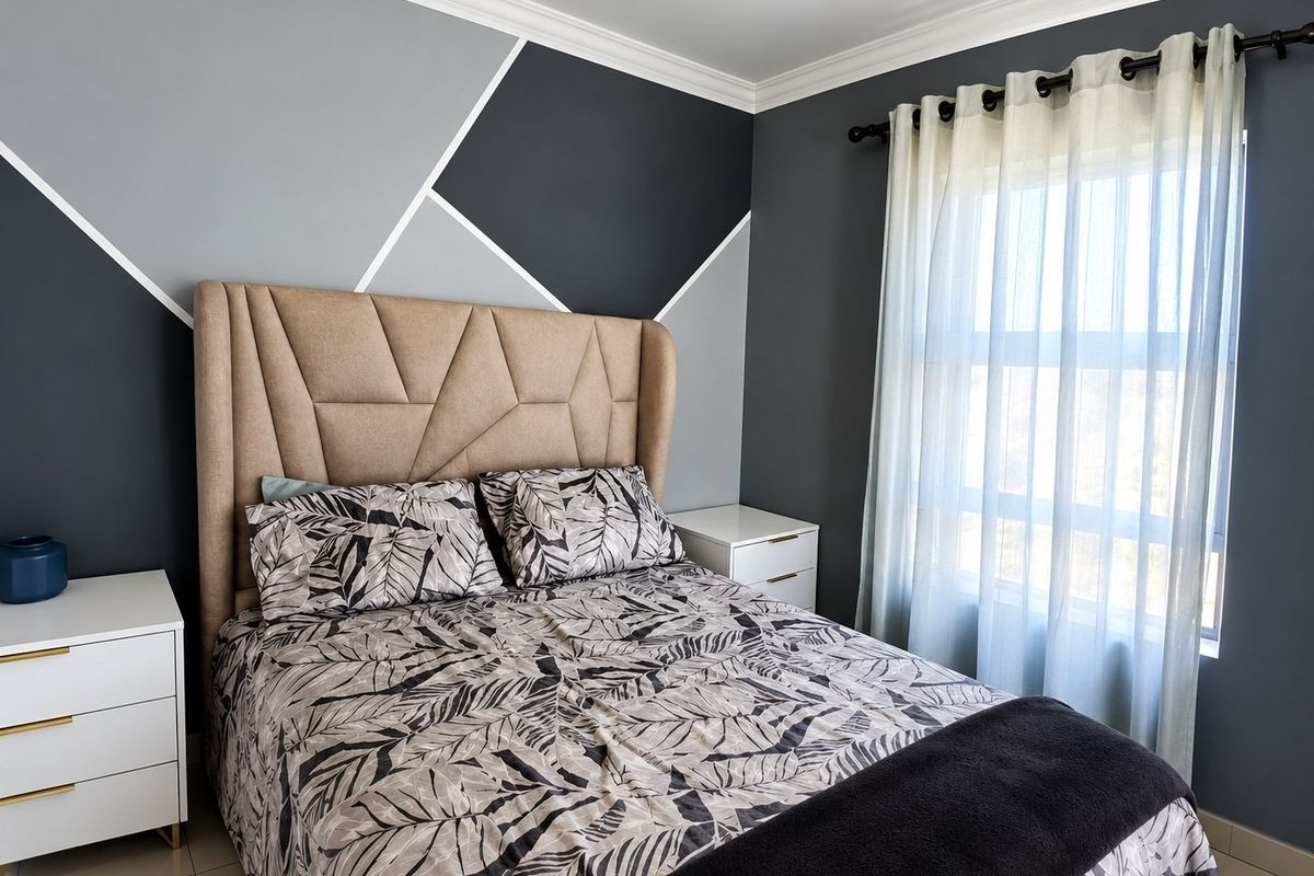 A well-maintained bedroom featuring modern geometric accent wall paint, crown molding, and tiled flooring with natural light from the window.
