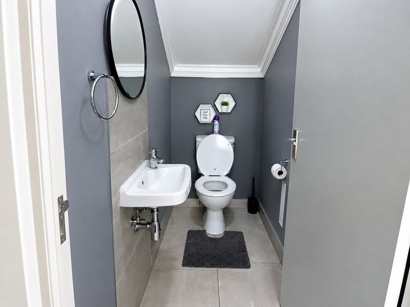 A compact, modern guest bathroom featuring a wall-mounted basin, toilet, neutral floor tiling, and contemporary grey wall finishes.