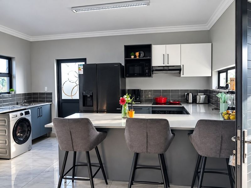 Modern kitchen featuring sleek grey cabinetry, stone countertops, a central breakfast island, and integrated appliances with a clean, contemporary aesthetic.