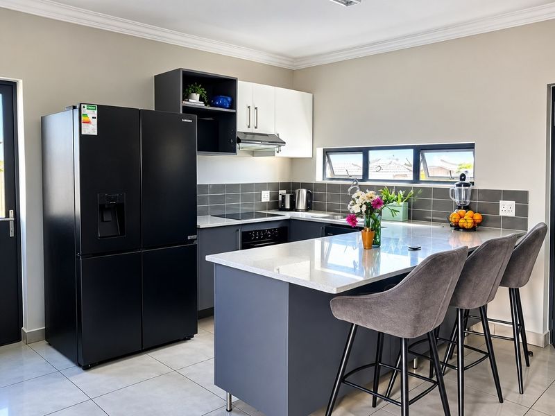 Modern kitchen featuring dark grey and white cabinetry, stone countertops, a central island with breakfast bar seating, and integrated appliances.