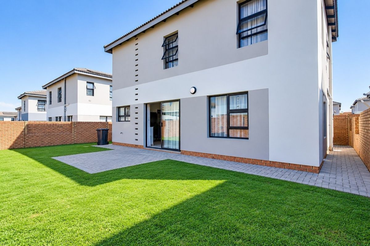 A well-maintained rear exterior view featuring a paved patio area, a neat lawn, and a brick boundary wall.