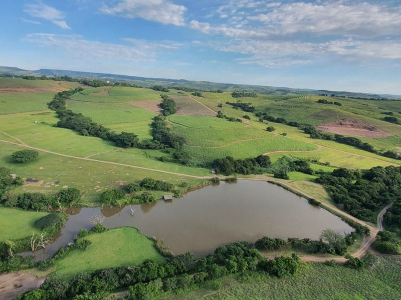 An aerial view of the small holding property featuring a large dam, expansive green pastures, and surrounding agricultural land.