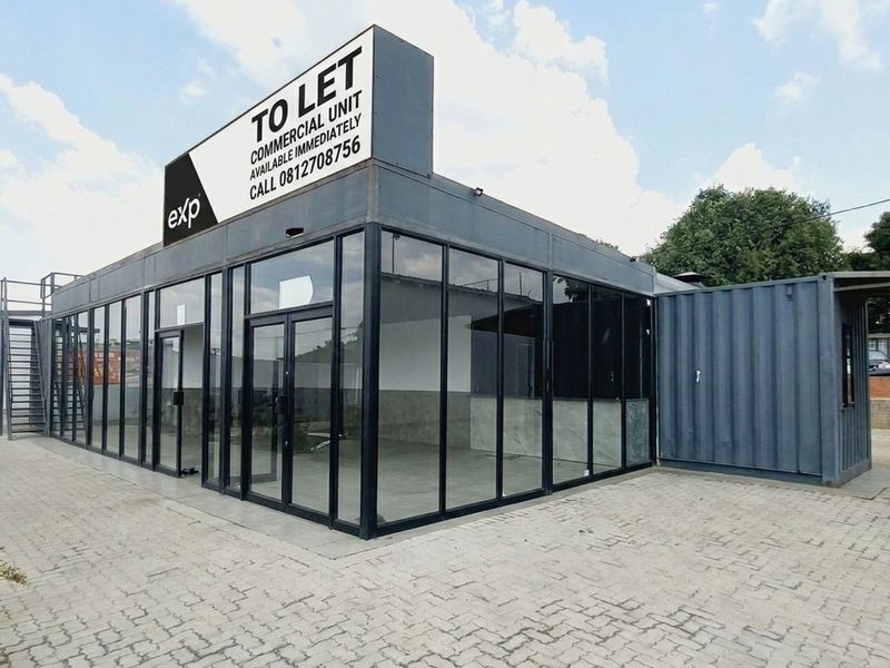 Modern commercial unit featuring a glass-fronted facade and shipping container construction, situated on a paved lot with prominent signage.