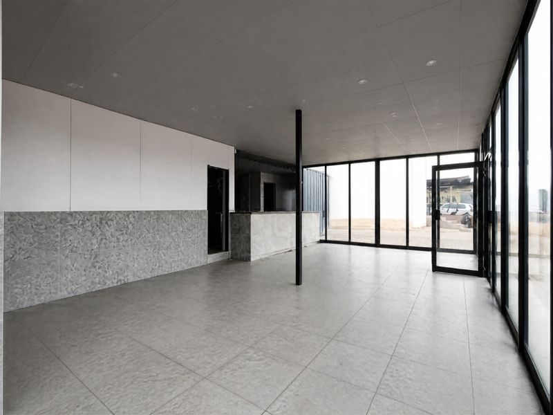 Modern open-plan commercial space featuring large glass windows, tiled flooring, recessed lighting, and a built-in service counter, offering a clean and versatile layout.