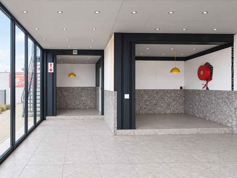 Modern open-plan commercial space featuring large glass windows, terrazzo-style tiling, recessed lighting, and integrated fire safety equipment.