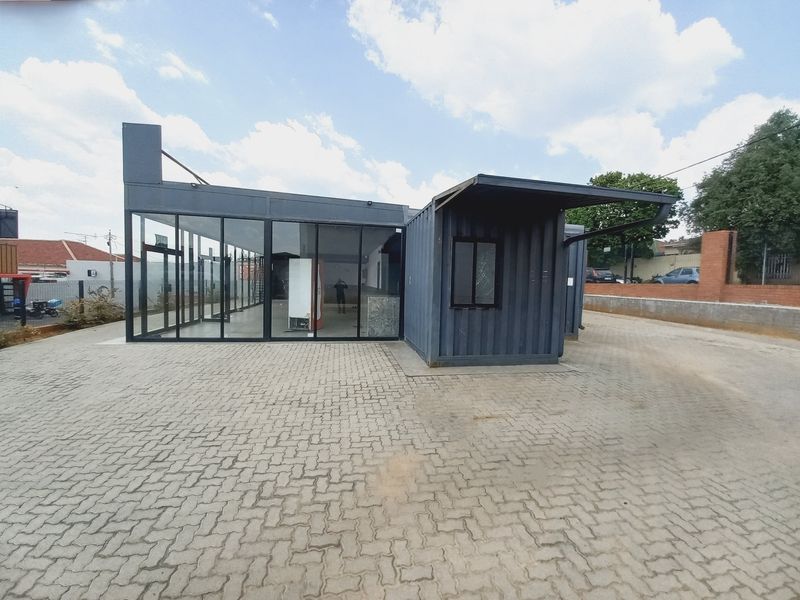 A modern commercial structure constructed from shipping containers featuring extensive glass paneling and a paved exterior area.