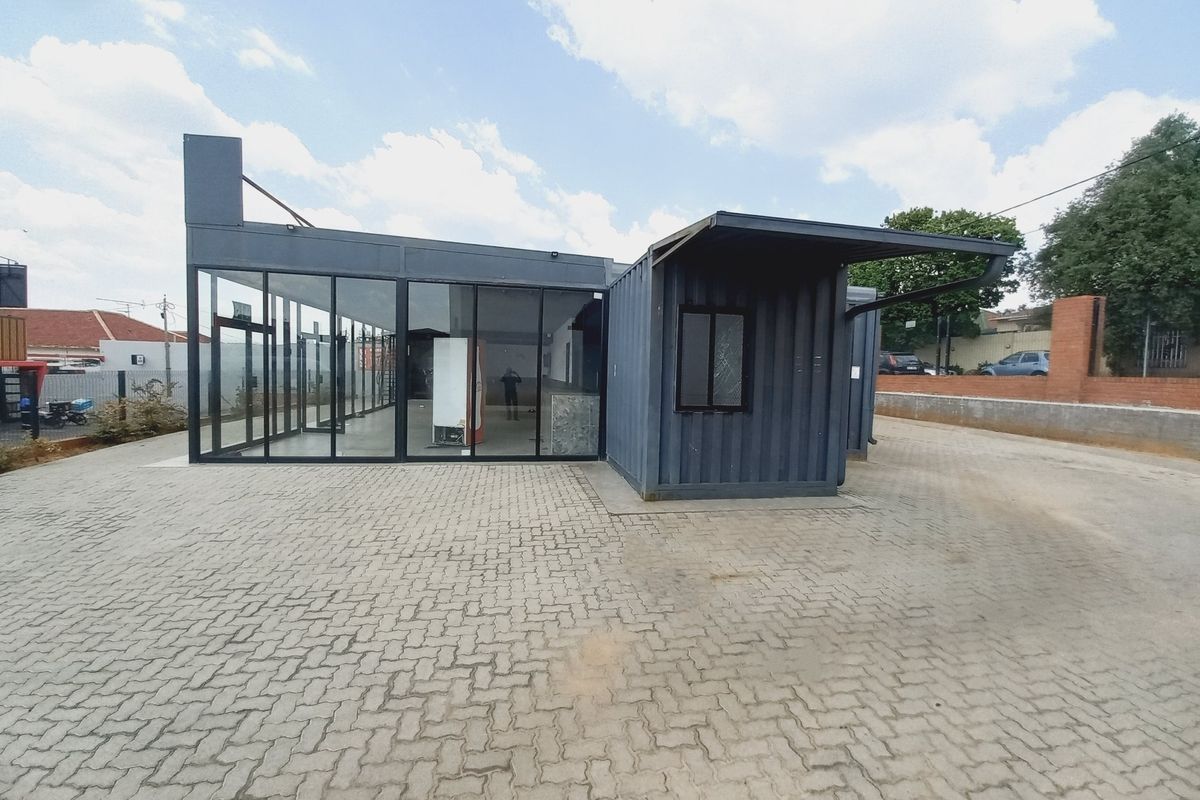 A modern commercial structure constructed from shipping containers featuring extensive glass paneling and a paved exterior area.