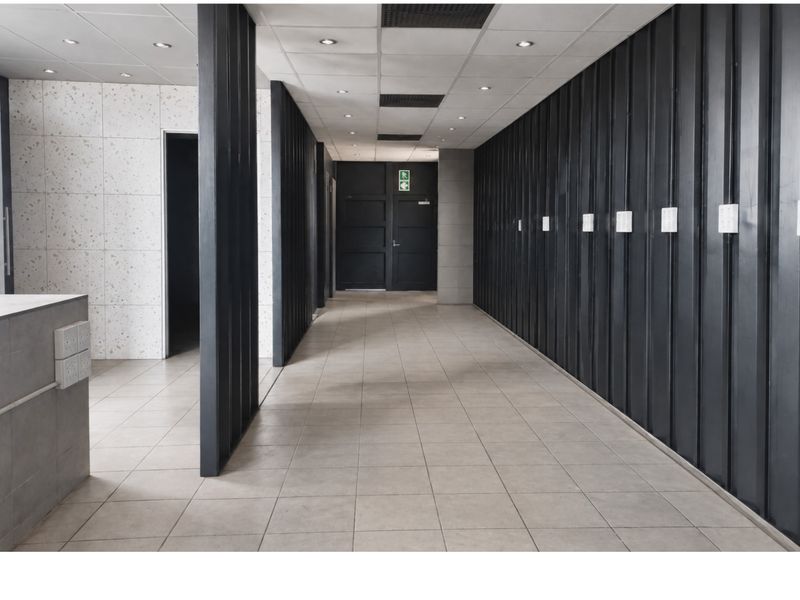 A modern commercial hallway featuring tiled flooring, a suspended ceiling with recessed lighting, and a combination of metal and terrazzo wall finishes.