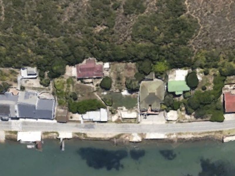 An aerial view of residential properties situated along a waterfront, showcasing the layout of the plots and surrounding coastal landscape.