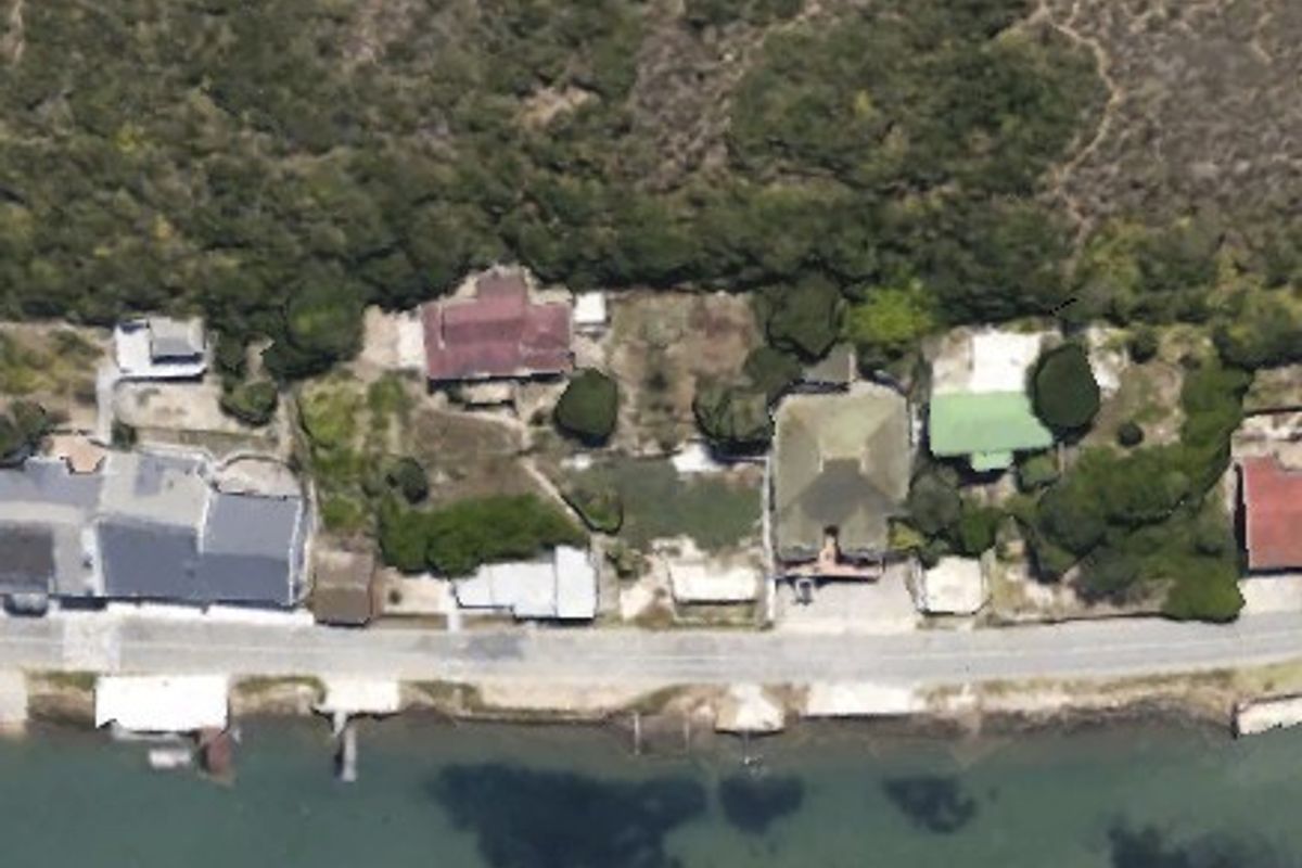 An aerial view of residential properties situated along a waterfront, showcasing the layout of the plots and surrounding coastal landscape.
