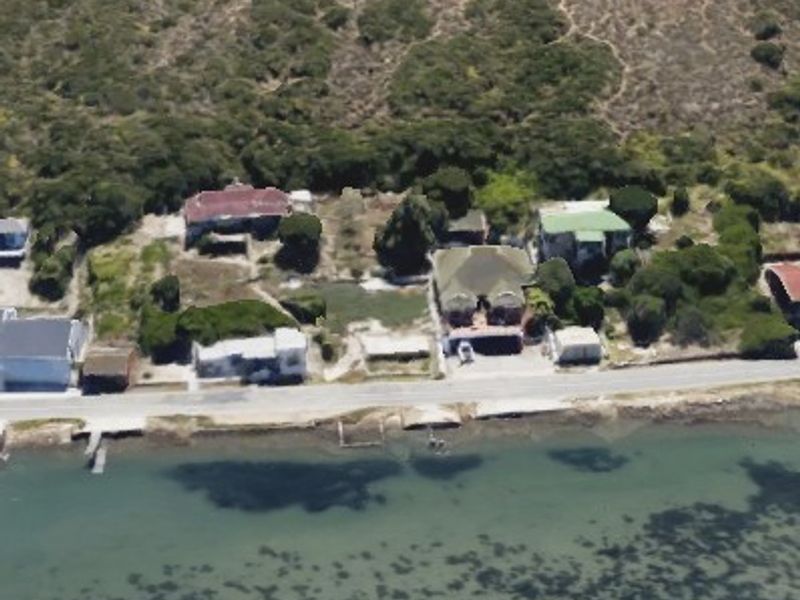 An aerial view of a coastal residential area featuring multiple properties situated along the waterfront with natural vegetation and direct access to the water.