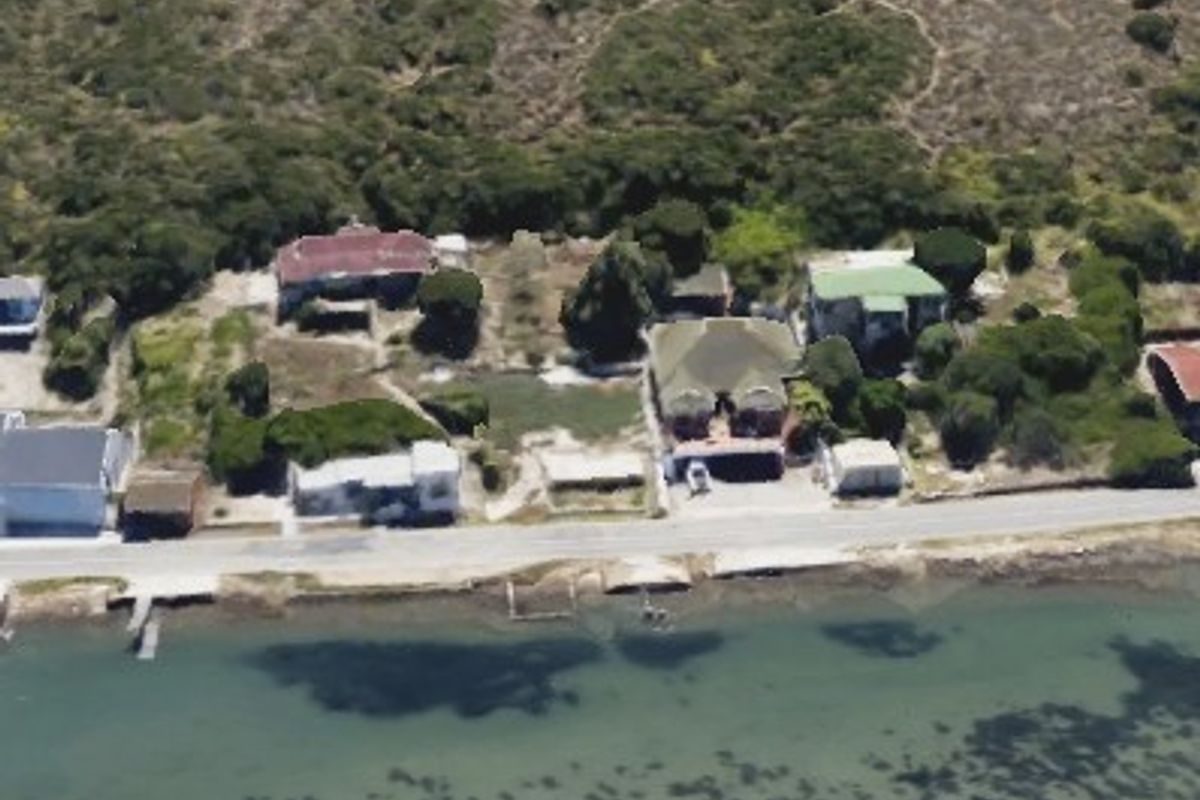 An aerial view of a coastal residential area featuring multiple properties situated along the waterfront with natural vegetation and direct access to the water.