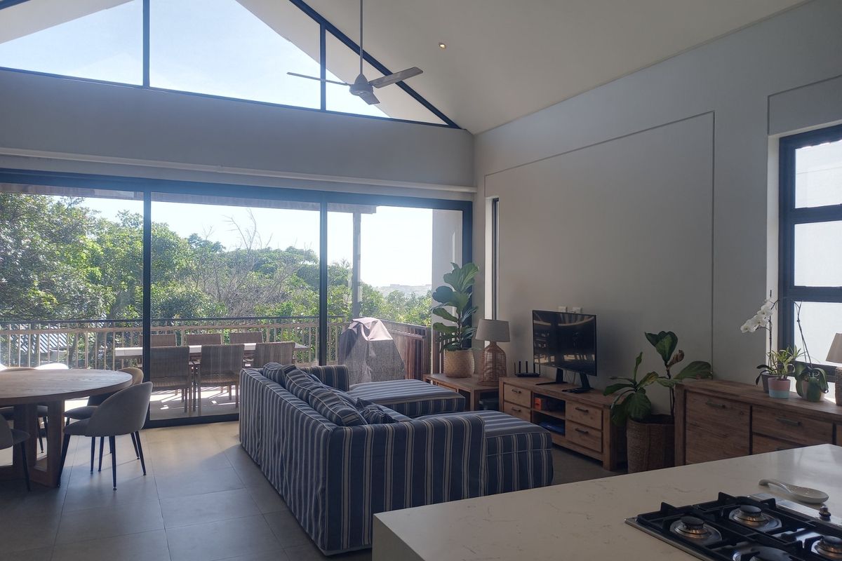 Spacious open-plan living area featuring a high vaulted ceiling, modern tiled floors, and large sliding doors opening onto a scenic outdoor deck.