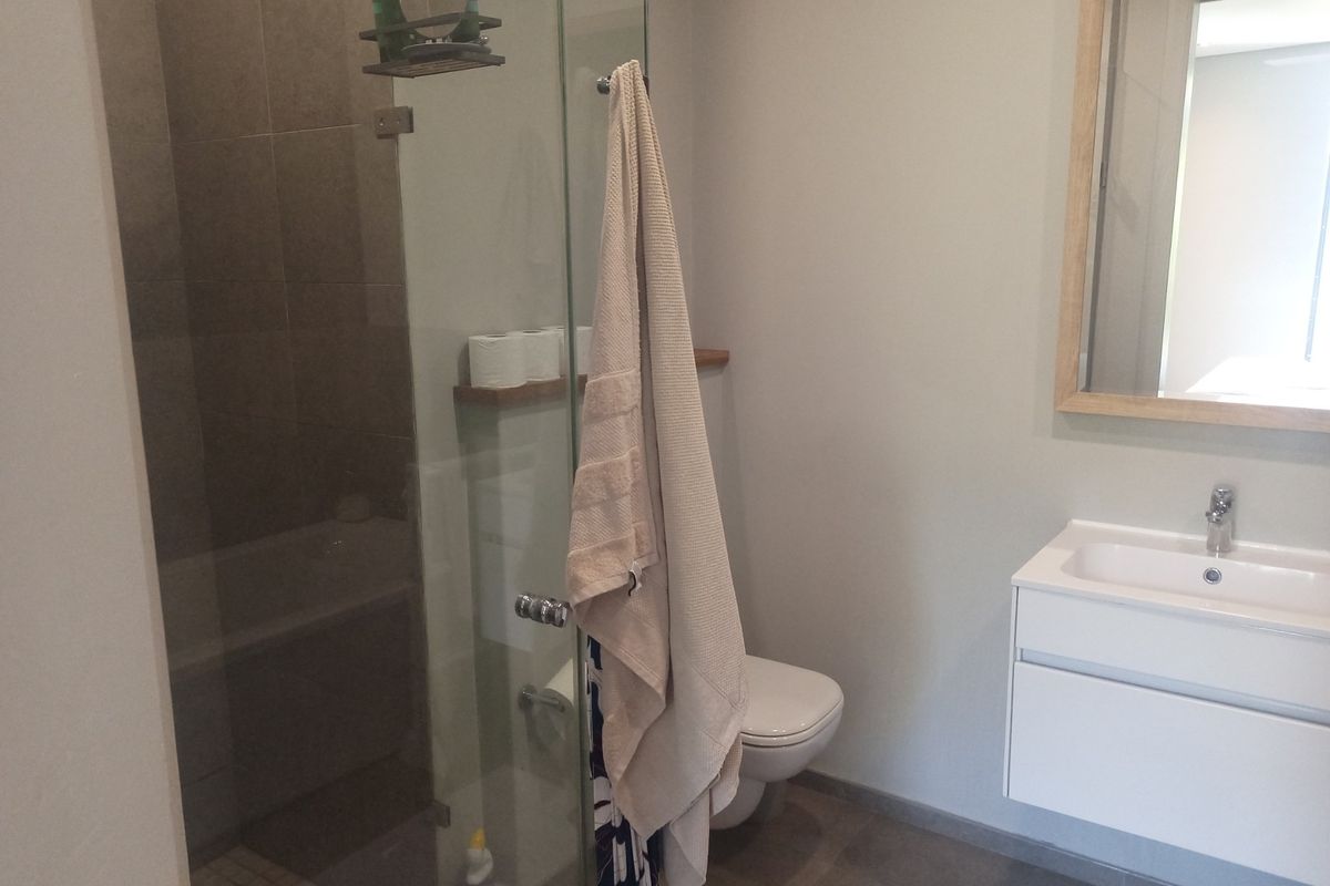 Modern bathroom featuring a glass-enclosed shower, wall-mounted vanity with basin, and a wall-hung toilet with neutral tiling.