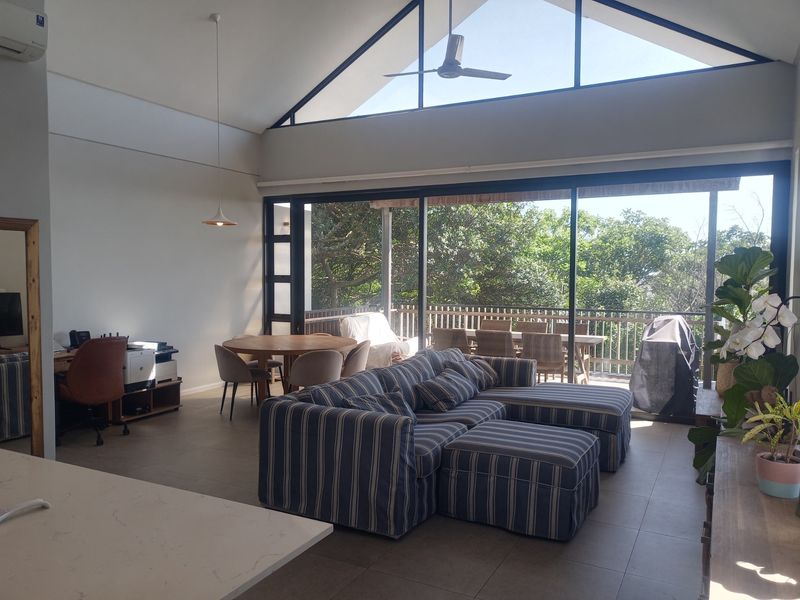 Spacious open-plan living area featuring a high vaulted ceiling, large sliding doors leading to a balcony, and abundant natural light.