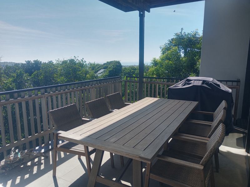 A spacious covered balcony featuring a timber balustrade and tiled flooring, offering an elevated outdoor area with scenic views.