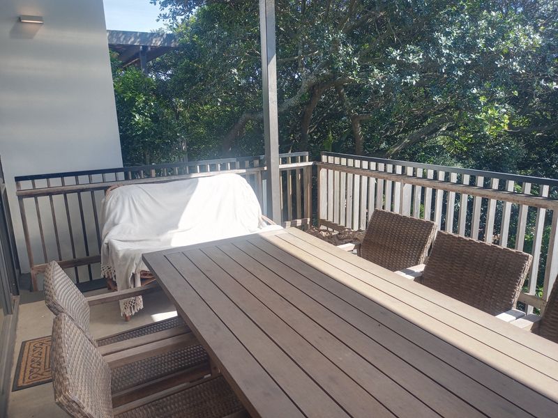 A covered balcony featuring a timber railing and concrete flooring, overlooking mature trees, providing a private outdoor space for relaxation.