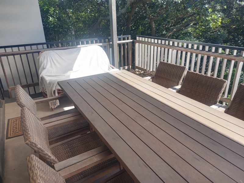 A covered outdoor balcony featuring a timber balustrade and concrete flooring, offering a functional space for outdoor dining and relaxation.
