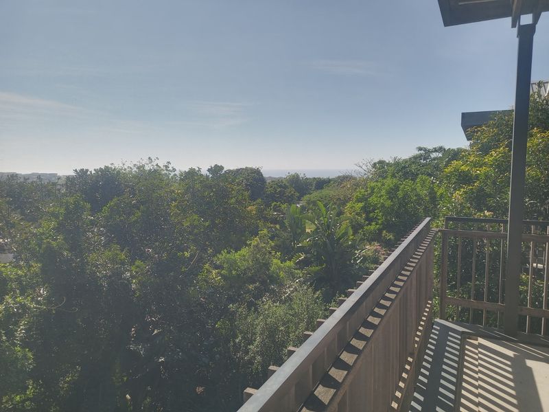 A balcony featuring a timber balustrade and concrete flooring, offering a scenic view of the surrounding lush greenery and distant horizon.