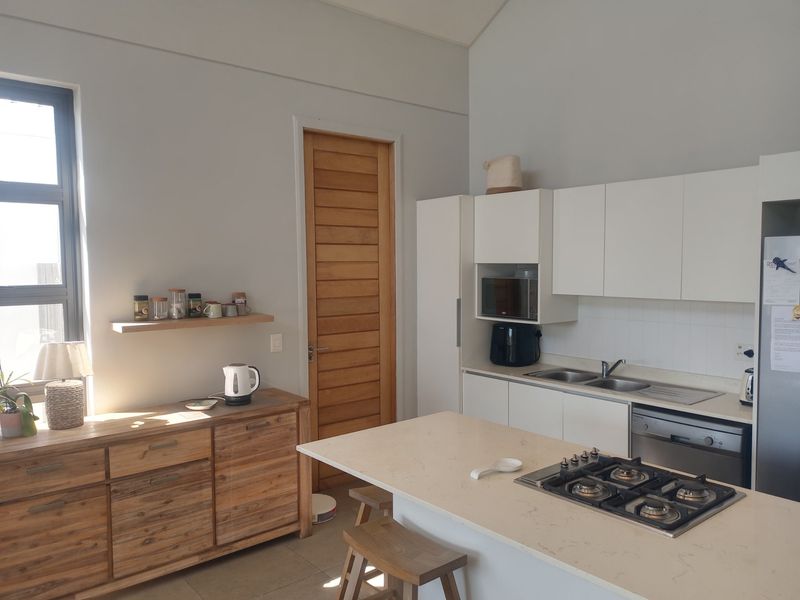 Modern kitchen featuring white cabinetry, stone countertops, a central island with a gas hob, and integrated appliances, complemented by neutral tiled flooring.