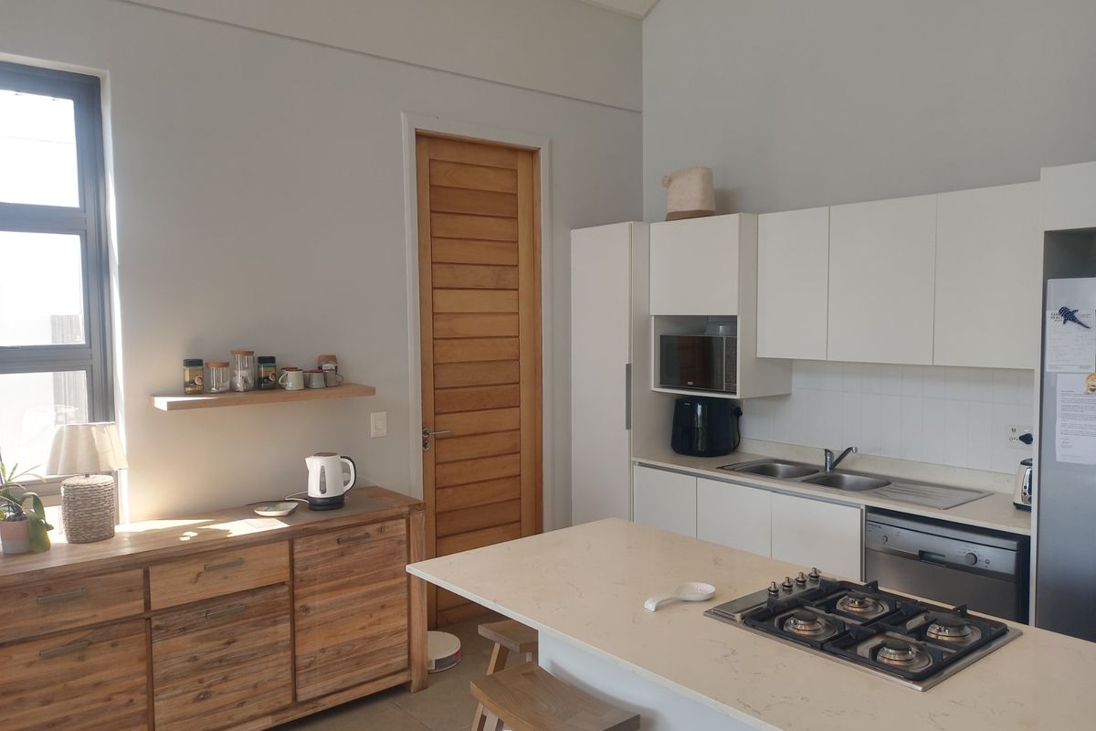 Modern kitchen featuring white cabinetry, stone countertops, a central island with a gas hob, and integrated appliances, complemented by neutral tiled flooring.