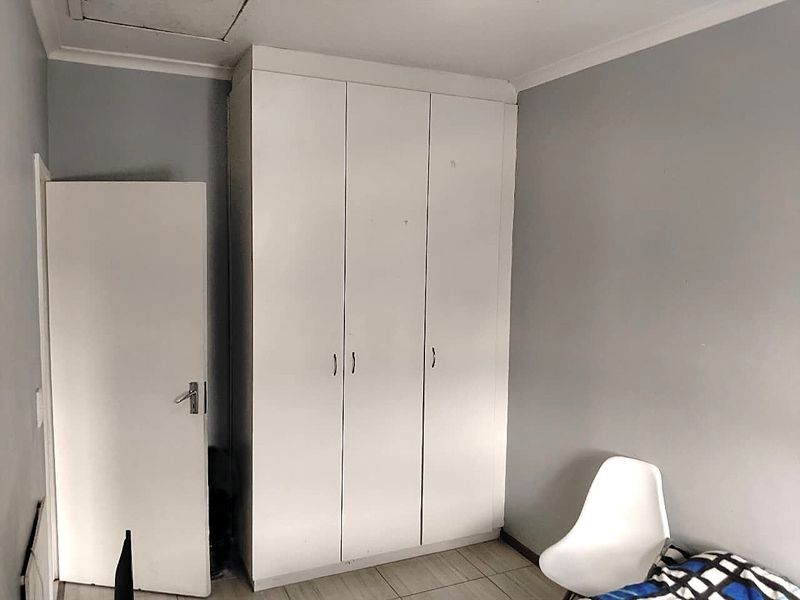 A bedroom featuring built-in white wardrobes, tiled flooring, and neutral grey walls, providing a functional storage solution within the living space.