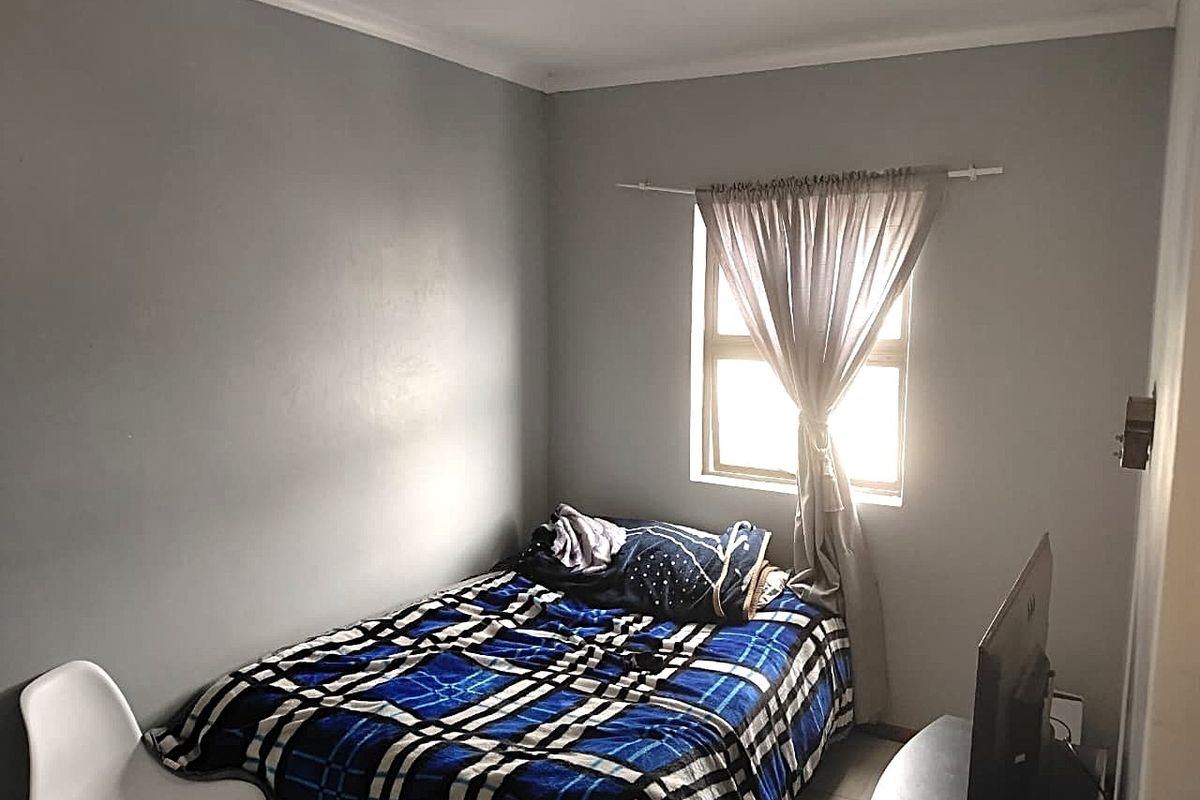 A compact bedroom featuring neutral grey walls and a single window, providing a functional space for rest.