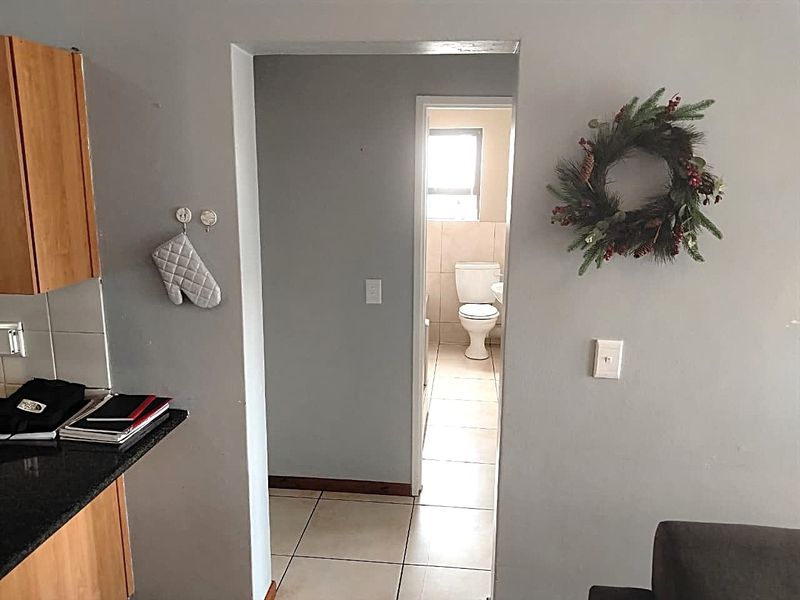 A view from the kitchen area looking through a hallway into a bathroom featuring tiled floors and standard fixtures.