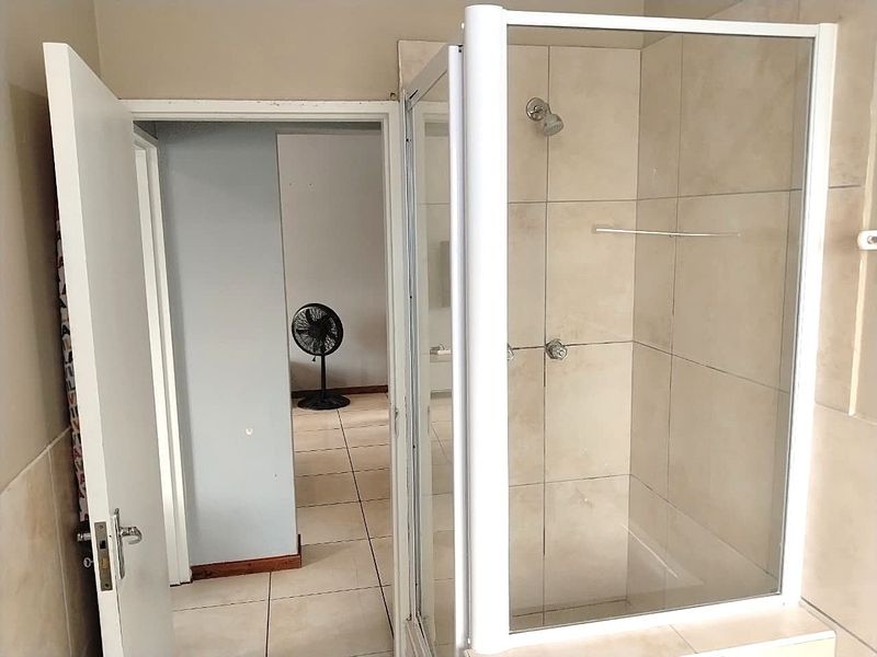 A functional bathroom featuring a glass-enclosed shower with neutral wall and floor tiling, providing a clean and practical space.