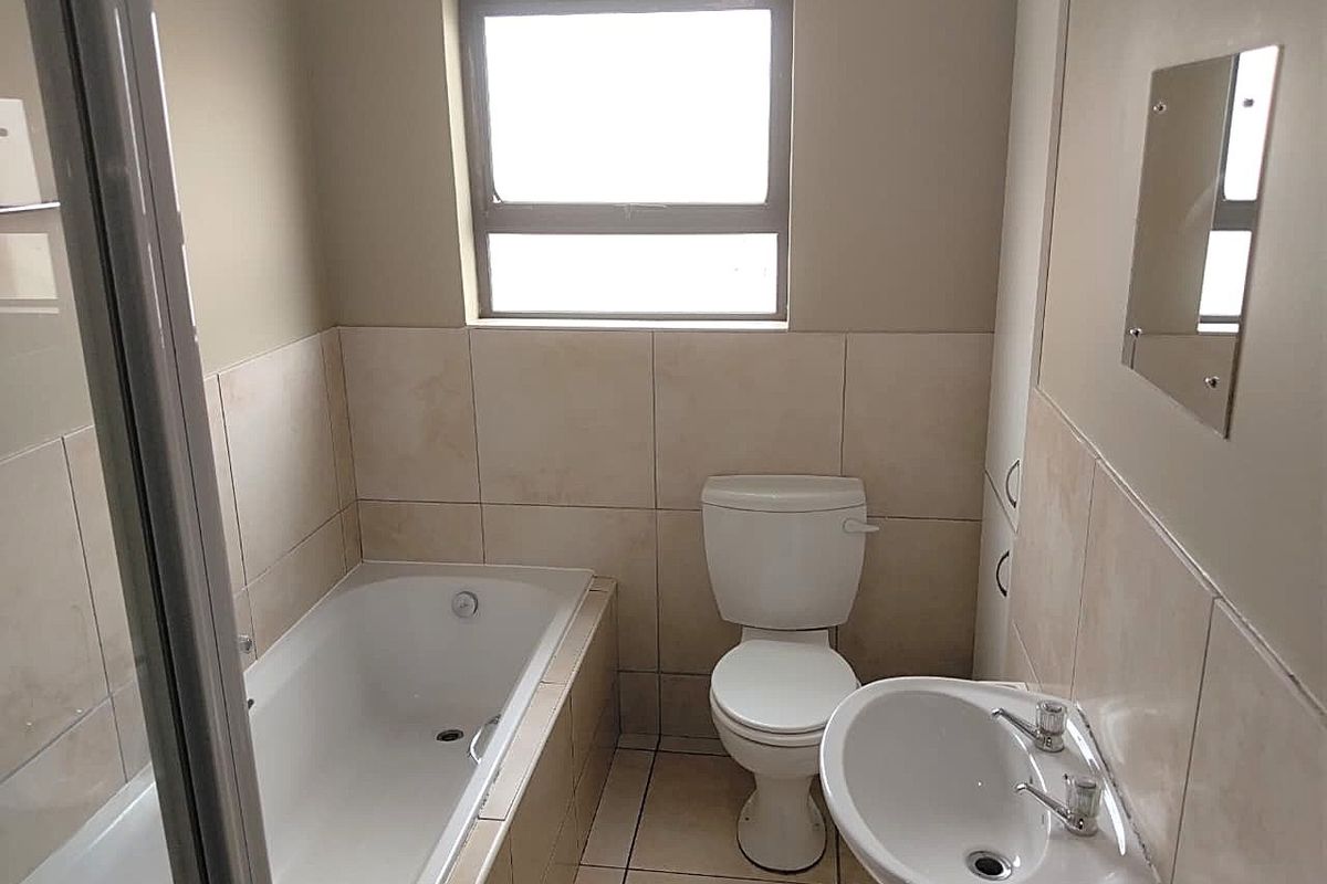 A functional bathroom featuring a built-in bathtub, pedestal washbasin, and ceramic toilet with neutral wall and floor tiling.