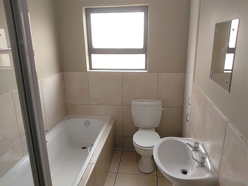 A functional bathroom featuring a built-in bathtub, pedestal washbasin, and ceramic toilet with neutral wall and floor tiling.