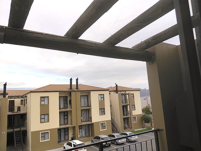 A view from a balcony featuring a timber pergola, overlooking the apartment complex grounds and parking area.