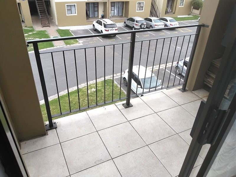 A functional balcony featuring tiled flooring and a secure metal balustrade, overlooking the apartment complex parking area.