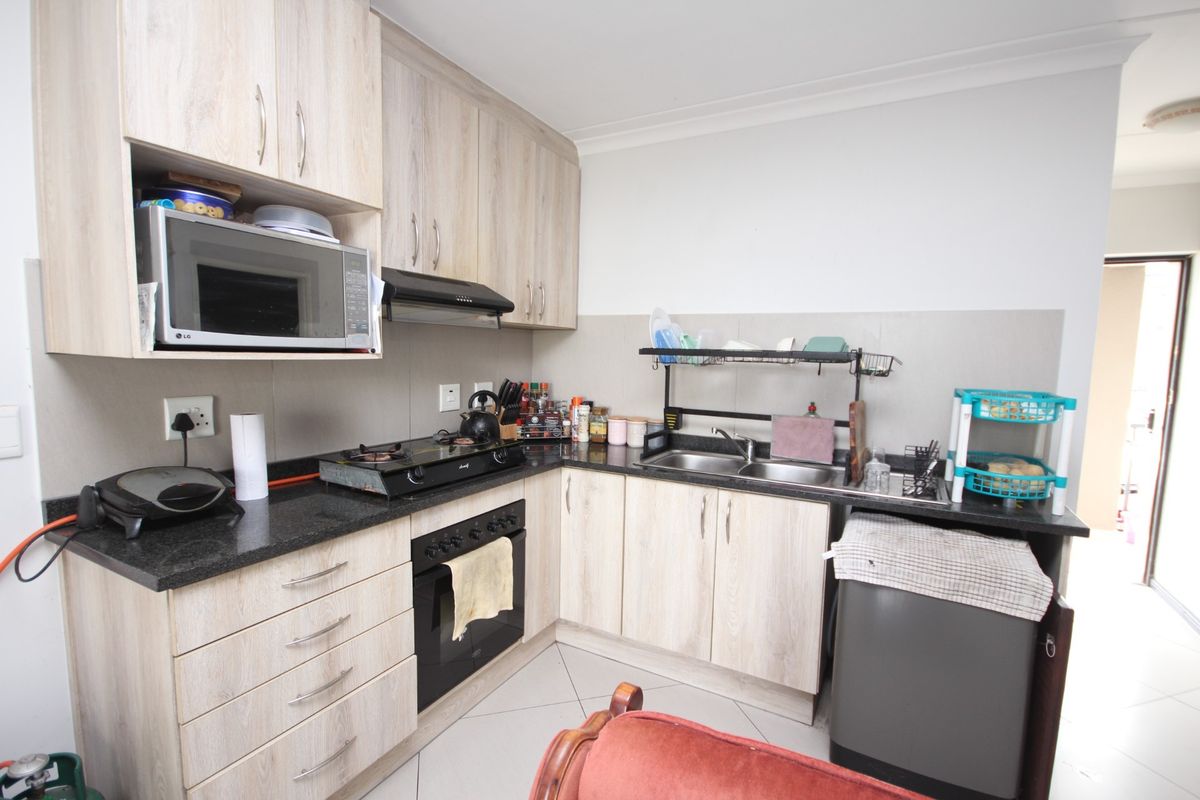 A functional kitchen featuring light wood-finish cabinetry, granite countertops, a built-in oven with gas hob, and a double sink with tiled backsplash.