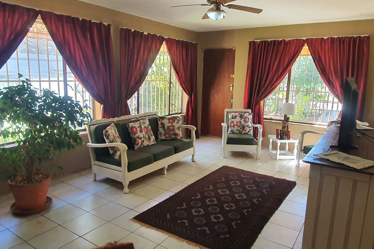 A living room featuring tiled flooring, a ceiling fan, and large windows fitted with security bars, providing natural light.