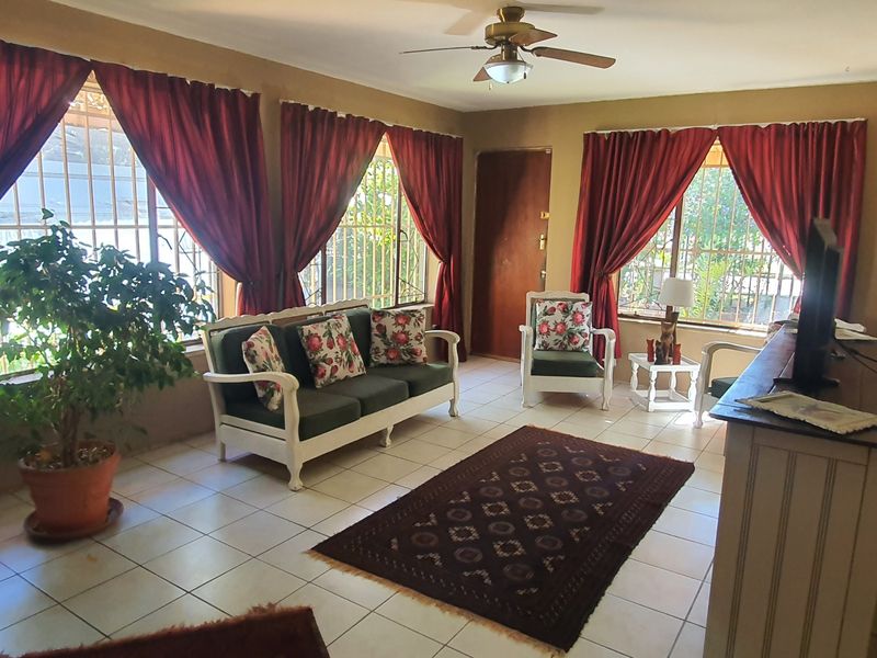 A living room featuring tiled flooring, a ceiling fan, and large windows fitted with security bars, providing natural light.