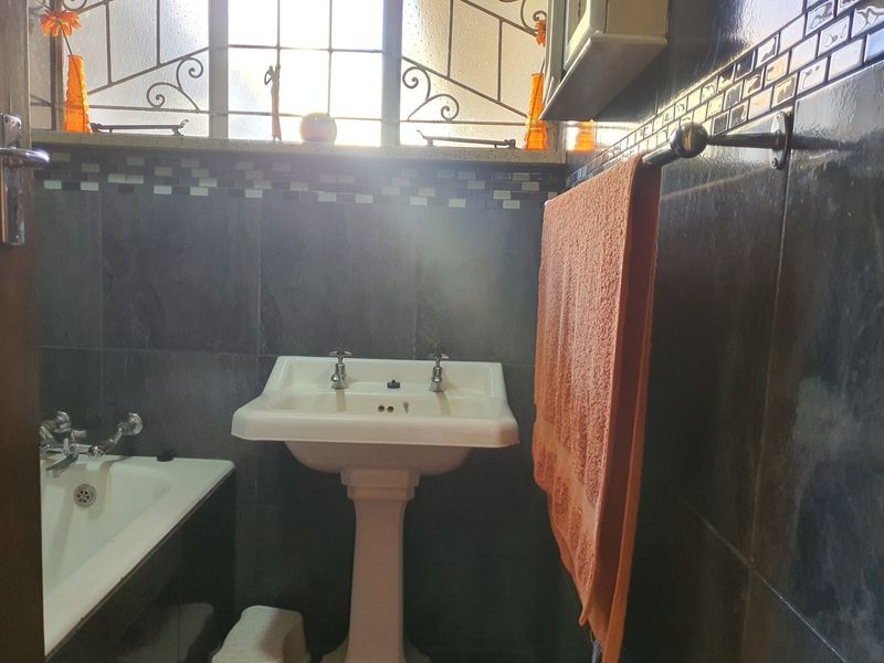 A functional bathroom featuring a pedestal basin, bathtub, and dark tiled walls with decorative mosaic accents.