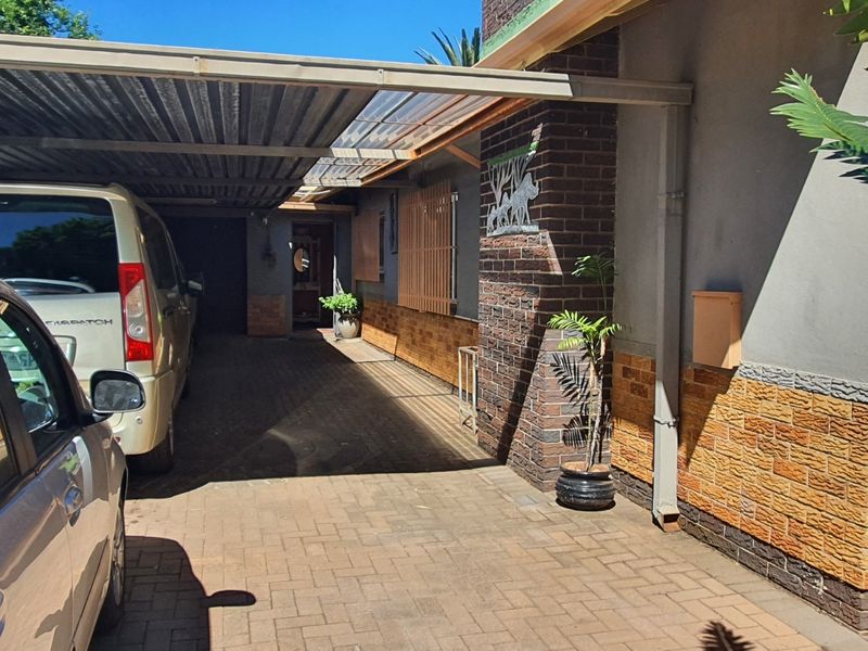 A paved driveway leading to a covered carport area with brick and plaster exterior wall finishes.
