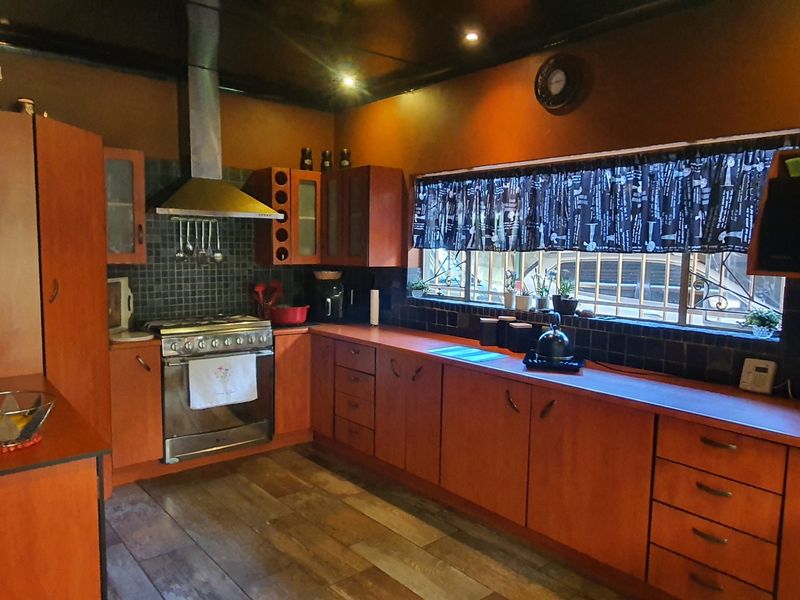 A functional kitchen featuring warm-toned wooden cabinetry, a stainless steel gas stove with extractor fan, and dark tiled backsplash with laminate flooring.