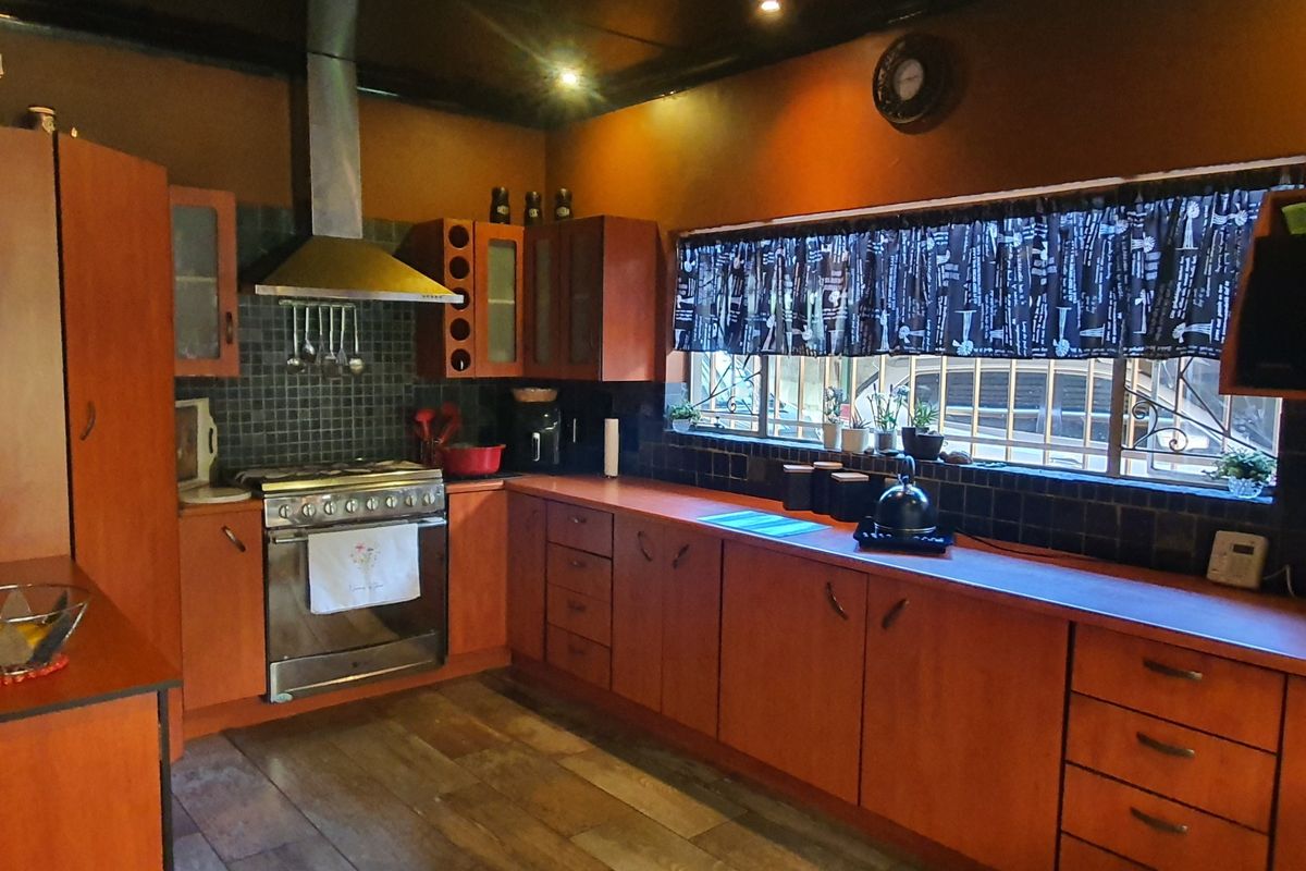 A functional kitchen featuring warm-toned wooden cabinetry, a stainless steel gas stove with extractor fan, and dark tiled backsplash with laminate flooring.