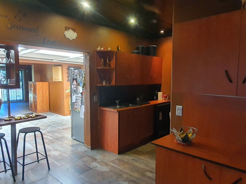 A functional kitchen area featuring built-in wooden cabinetry, a double sink, and tiled flooring, with an open-plan layout leading to an adjacent living space.